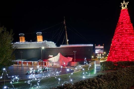 The exterior of the the ship shaped Titanic Museum at night with a giant red Christmas Tree and stars made of wires and light in front of it.