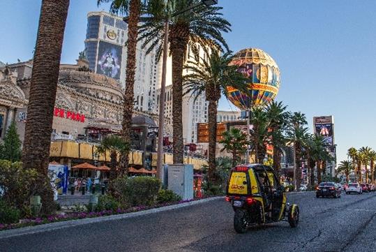 A yellow GoCar driving down the Las Vegas Strip with cars in front of it and the city in the background.