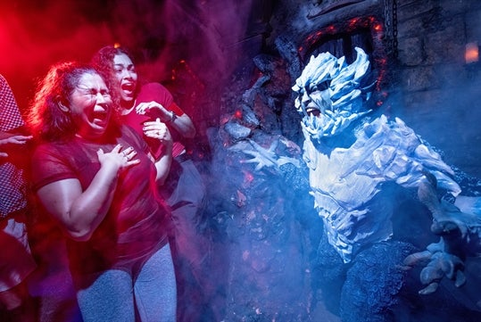 Two guests react with a scream as they encounter a scareactor dressed in costume in the "Dueling Dragons" haunted house.