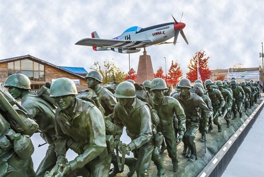 The P-51 "Donna K" soars above the "Storming the Beach" bronze statue.