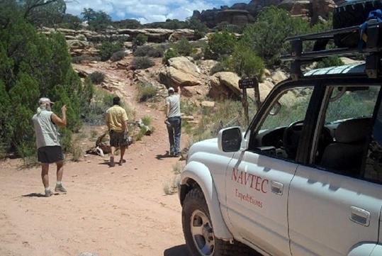 A white NAVTEC SUV parked with hikers on their way to start their White Rim Trail in Canyonlands National Park.