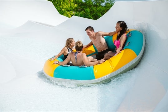 An adult and three children in a blue and yellow tube splashing on Ohana Falls at White Water in Branson, Missouri.

