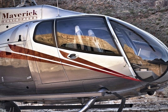 A silver and red Maverick Airbus helicopter featuring its wrap-around glass for outstanding visibility with rocks in the background.