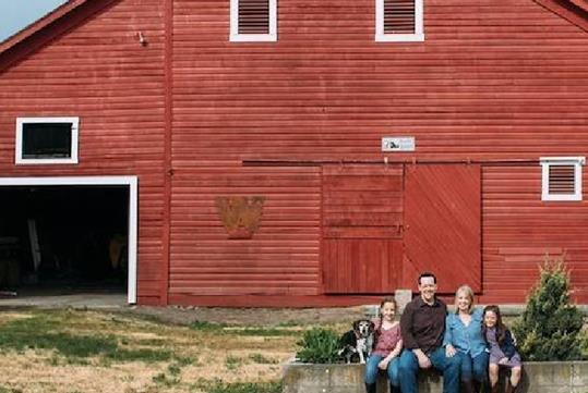 A family of four and their dog sitting outside a large red barn at the Armstrong Family Winery near Seattle, Washington.