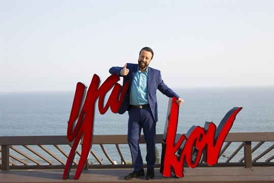 Yakov Smirnoff standing in front of a large red Yakov sign