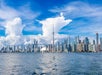 Toronto skyline with the CN Tower and modern skyscrapers, viewed from across the water under a blue sky with large clouds.