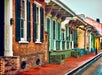 A row of colorful, historic brick and wooden houses with shutters and decorative details line a wet street.