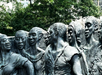 A bronze sculpture depicting a group of figures standing closely together, set outdoors with trees in the background.