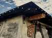 Exterior of Lafitte's Blacksmith Shop Bar, with a rustic sign and string lights. Brick and stucco walls are visible under a partly cloudy sky.