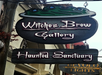 Sign for "Witches Brew Gallery" and "Haunted Sanctuary" with a cauldron graphic above on a street.