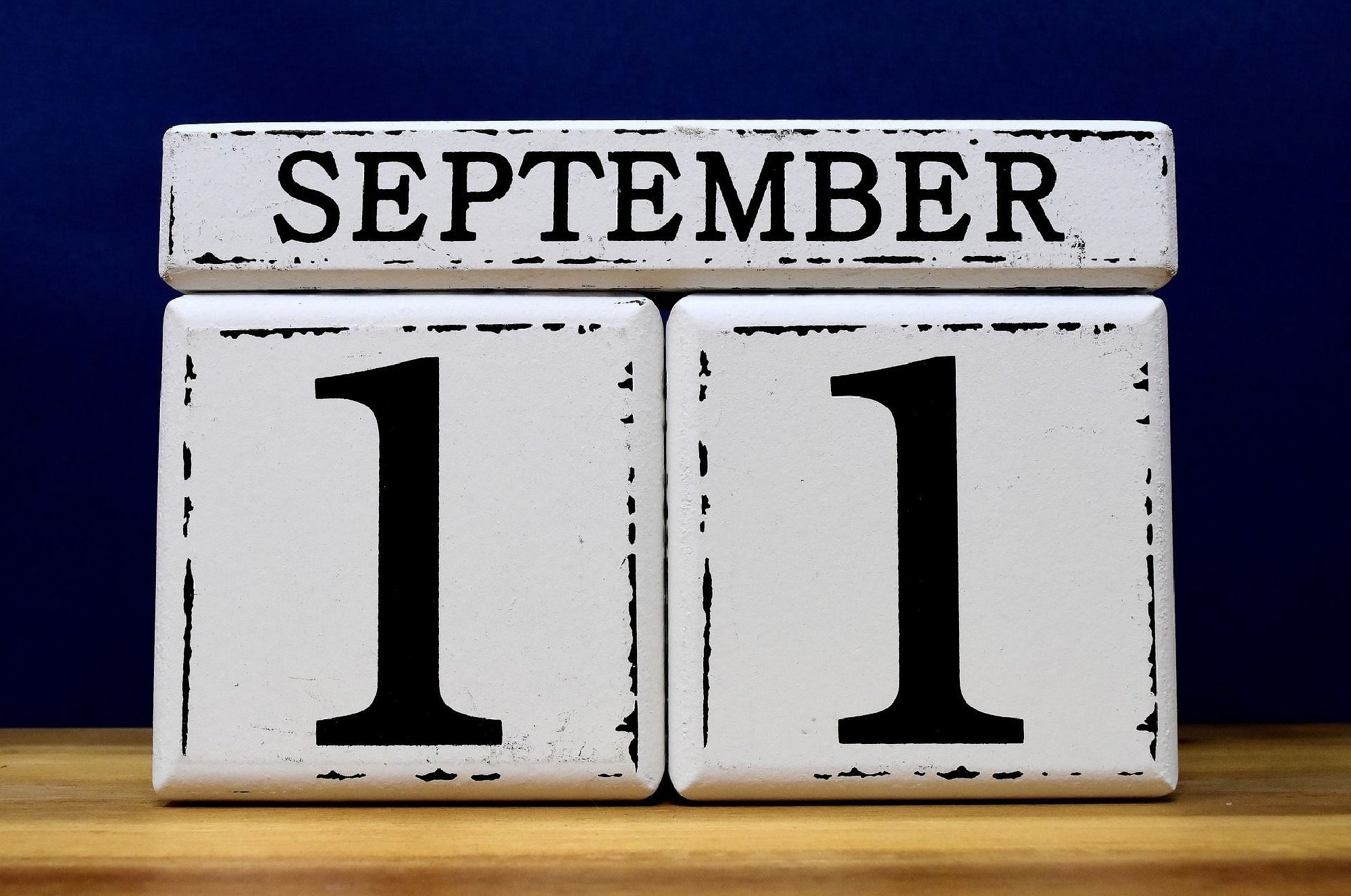 White wooden blocks display "September 11" against a dark blue background, with the date shown in large black numbers and letters.