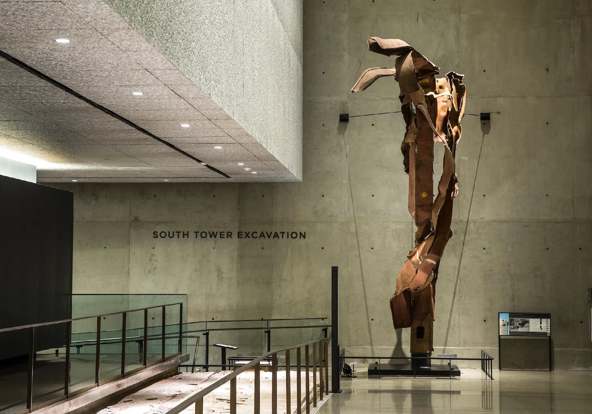 A large twisted steel beam sculpture stands in a modern concrete museum space labeled "South Tower Excavation.
