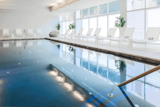 A relaxing indoor pool surrounded by large windows and sun loungers.