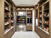 A modern convenience store with wooden shelves stocked with drinks, snacks, and grocery items. Central section features a glass-front refrigerator with various beverages.