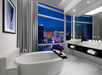 Large marble-tiled bathroom with a soaking tub, floor-to-ceiling windows with views of Planet Hollywood and the Strip.