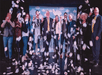 A few audiences on stage happily posing with Adam London while playing cards as confetti falls around them after the show.