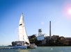A white sailboat passes by Alcatraz Island with its historic prison buildings and water tower under a clear blue sky.