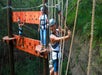 Three people wearing helmets and harnesses cross a ropes course suspended among trees, smiling and navigating various obstacles.