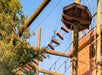 Wooden high ropes course with suspended platforms and obstacles, surrounded by trees, under a clear blue sky.