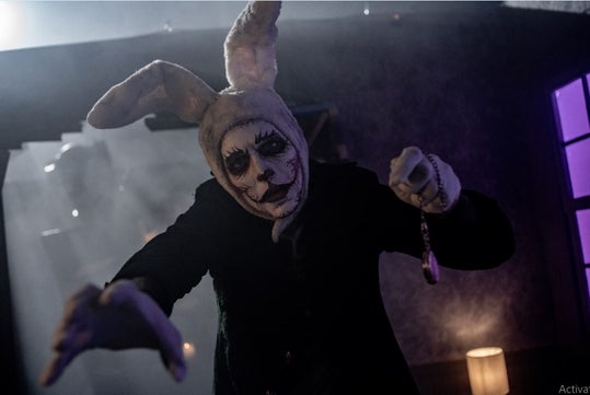 A menacing figure in a bunny costume with a grotesque face, extending its arms in a dark, foggy setting, creating a sense of horror.