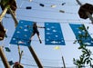 A person in climbing gear navigates a suspended obstacle course with blue panels and a clear sky in the background.