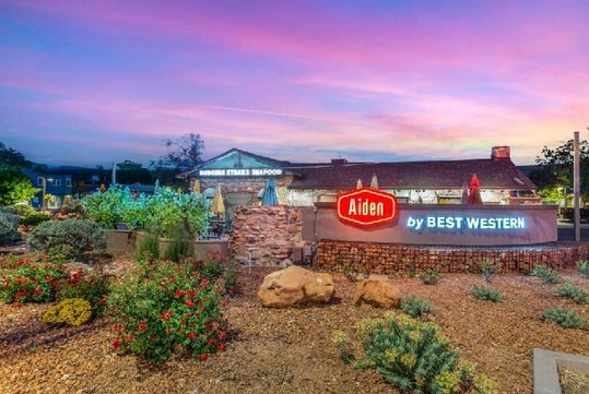 The neon sign for the Aiden by Best Western with nice landscaping around it and the hotel in the background at sunset.