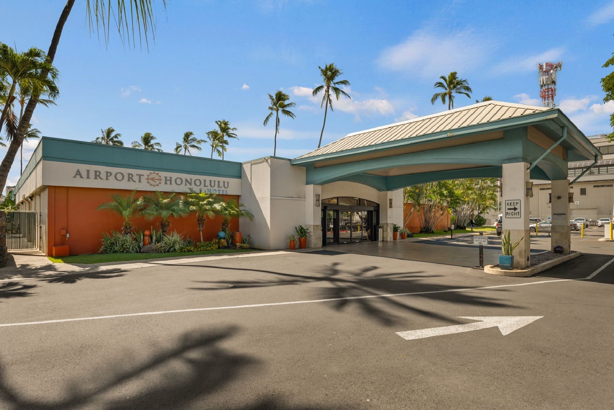The exterior entrance of Airport Honolulu Hotel with palm trees, a covered driveway, and clear blue sky.