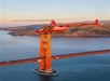 A bright red helicopter flying past the Golden Gate bridge at sun set on the Alcatraz and San Francisco Sites Helicopter Tour.