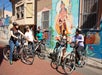 Group of people on bicycles stopped near a colorful mural on a city street, with one person pointing at the artwork.