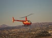 A red and white helicopter with tail number N429RH flies above a sprawling cityscape with hills in the background.