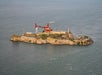 Aerial view of Alcatraz Island with a red helicopter flying overhead and the surrounding ocean.