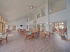 Spacious dining area with wooden tables and chairs, a high ceiling, large windows, and a long hallway leading to other rooms.