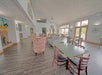 Spacious dining area with wooden tables and chairs, upholstered armchairs, large windows, and a brick fireplace.