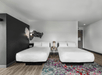 A hotel room with two white queen beds, a night stand, a multicolored rug, and a black accent wall.