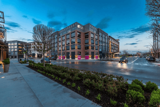 Street view looking at the brick exterior of the Aloft Columbus Easton with cars driving by at dusk on a cloudy night.