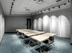 A meeting room with gray walls, blue carpet, and several tables pushed together with chairs on the sides.