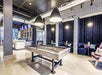 Modern lounge area with a pool table in the center, bar seating in the background, and booths with dark cushions along the wall.