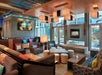 Modern lounge area with contemporary furniture, colorful cushions, a fireplace, and overhead square lights. Large windows provide natural light. A decorative art piece adorns the wall.