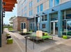 Modern outdoor patio area with green seating, a stone wall, and cube-shaped lights, adjacent to a tall building with large windows.