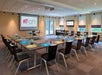 A modern conference room with a U-shaped table arrangement, screens displaying the "Aloft" logo, and neatly arranged chairs. The room is well-lit with large windows and overhead lighting.