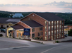 A multi-story brick hotel with an entrance canopy, surrounded by a parking area and greenery, under a cloudy sky at dusk.