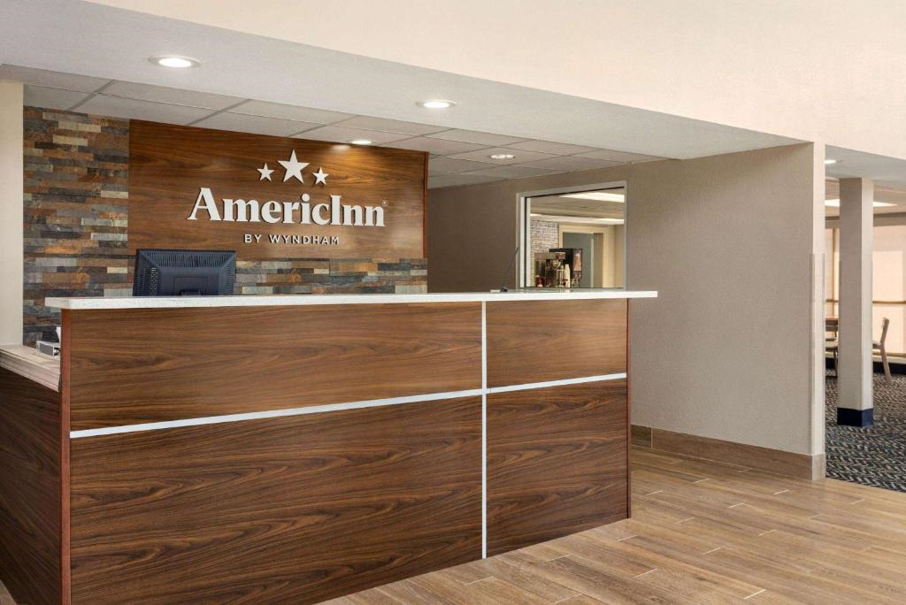 Hotel reception area with a wooden front desk and a sign reading "AmericInn by Wyndham" on the wall behind.