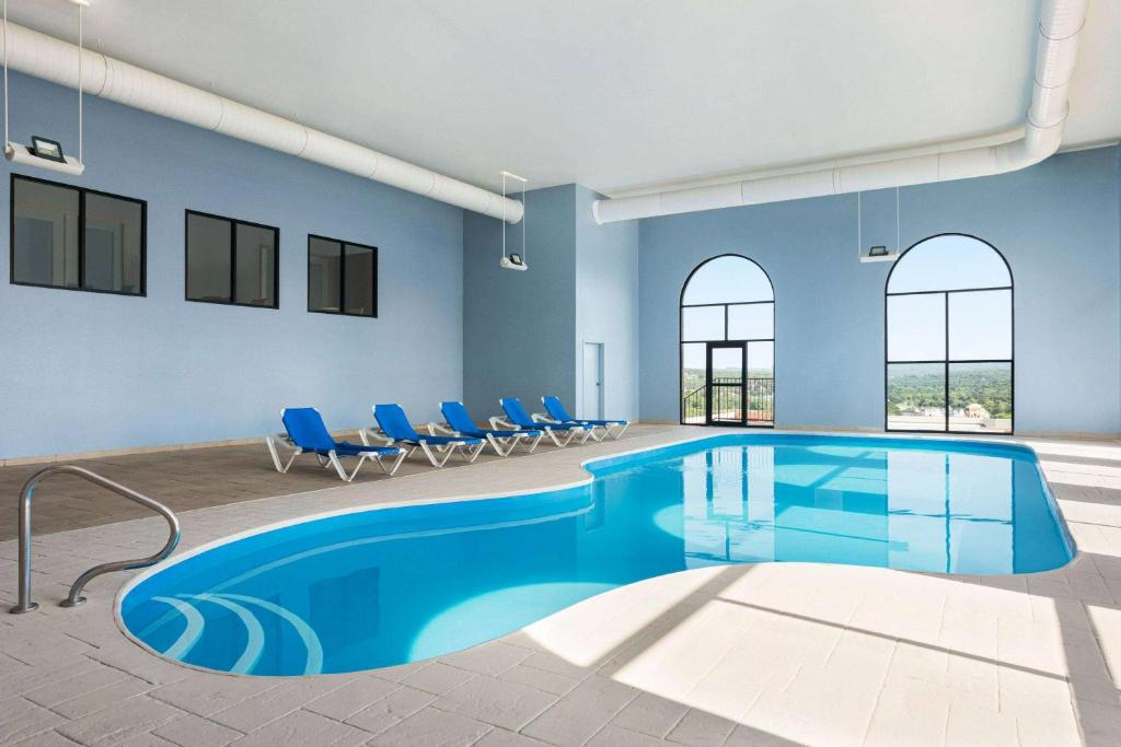Indoor swimming pool with blue lounge chairs along the side, large arched windows, and a view of the outside.