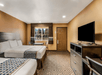 A hotel room with two queen beds, a table and two chairs, and a dark brown dresser with a tv sitting on it.