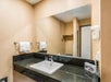 A hotel room bathroom sink with a large mirror above it, a hair dryer on one wall, and a towel rack on the other.