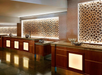 Hotel reception area with wooden counters and illuminated decorative wall panels featuring a honeycomb pattern.