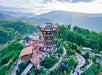 Aerial view of an observation tower surrounded by landscaped gardens and buildings, set against a backdrop of forested hills and mountains.