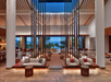 Spacious modern lobby with large windows, tall pillars, and a sea view. Minimal furniture includes sofas and stools.