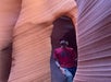 Person in a red shirt and cap stands inside a narrow slot canyon with textured, wavy sandstone walls.
