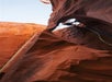 A person climbs a steep canyon with ropes and equipment, surrounded by tall, smooth red rock formations under a clear blue sky.